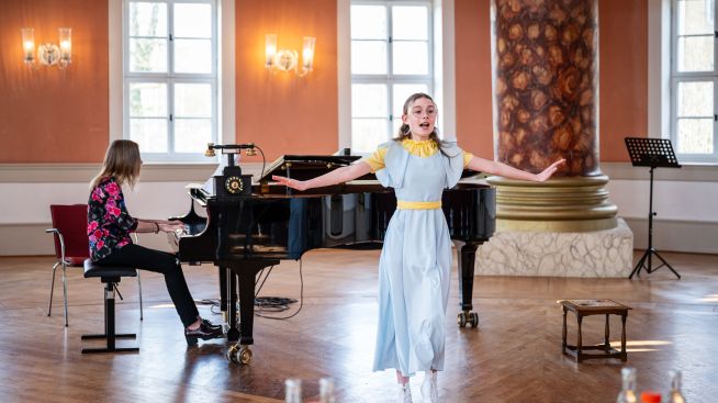 Junge Musicalsängerin in blauem Kleid vor Flügel und Pianistin singt im Achteckhaus