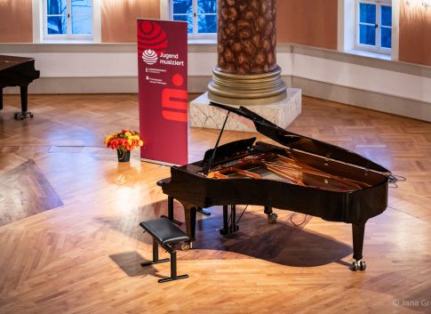 geöffneter Flügel im festlich beleuchteten Saal vor einem Roll-up von Jugend musiziert und einer Vase voller Blumen