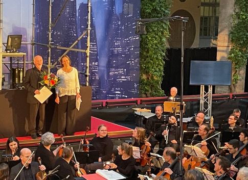 Präsidentin des LMR und Ehrennadelträger Dr. Bickner mit Blumenstrauß auf der Bühne hinter dem Orchester