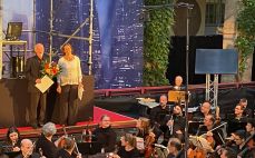 Präsidentin des LMR und Ehrennadelträger Dr. Bickner mit Blumenstrauß auf der Bühne hinter dem Orchester